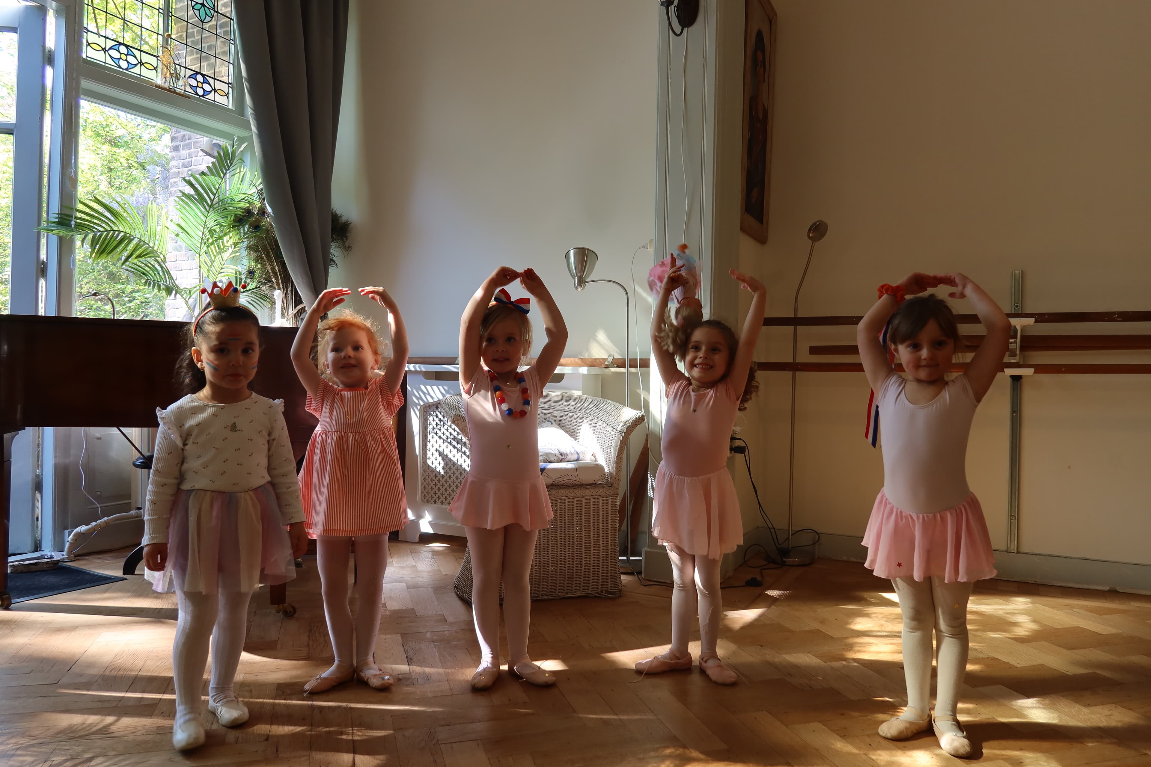 Five little girls in pink tutus with arms raised at Arabesque Studio